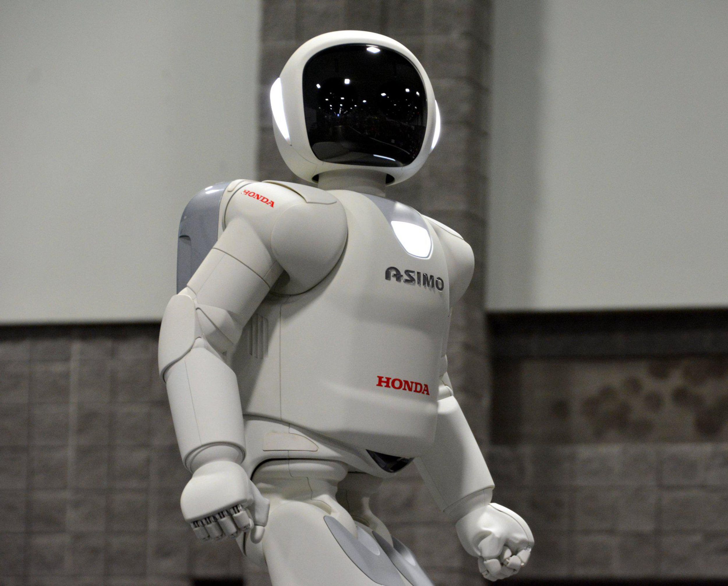 A white humanoid robot with a black helmet stands facing the camera