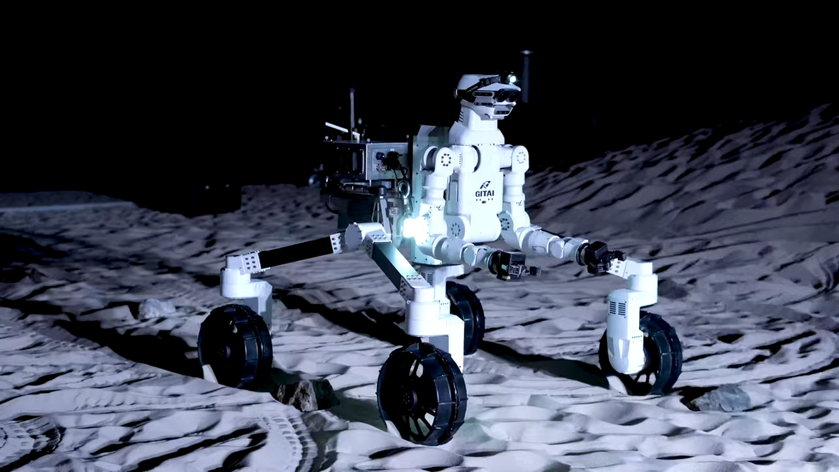 A white humanoid robotic torso mounted on a four wheel bogey system rolls across a simulated lunar surface