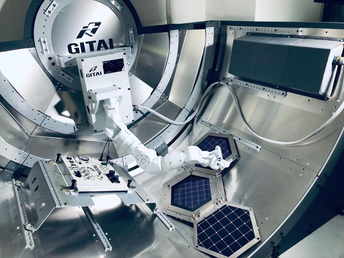 A white robot arm assembles hexagonal solar panels inside of a test model of an ISS airlock