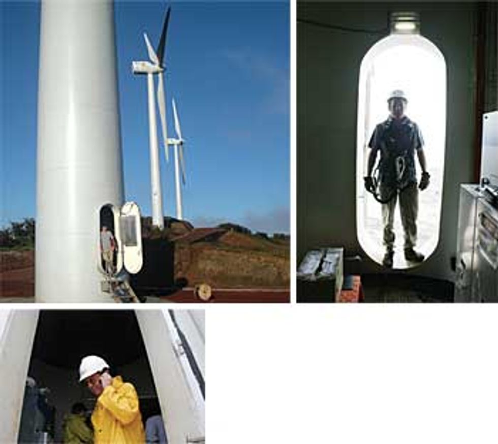 A wind turbine with a small door where a man stands and another speaks on his cellphone