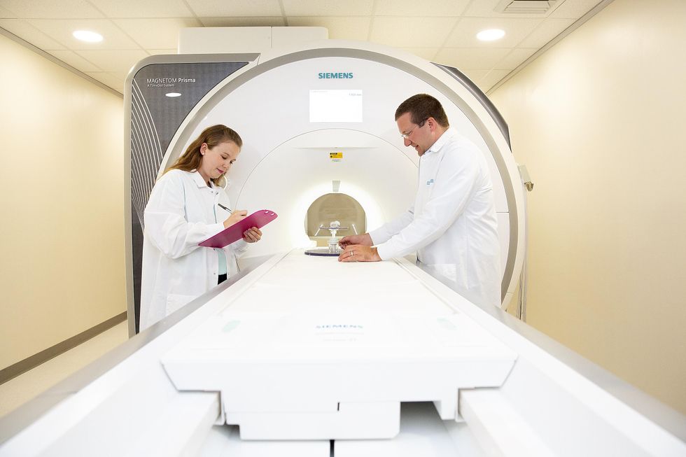 A woman and a man in medical aprons next to a MRI machine.