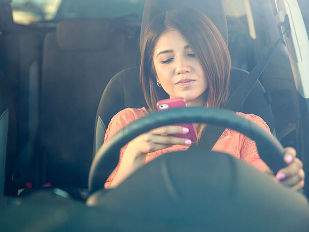 A woman behind the wheel of a car looking at a smartphone
