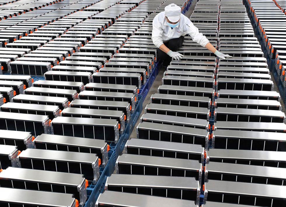A worker inspects rows of electric vehicle batteries.