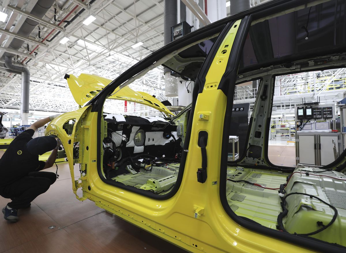 A worker works on the frame of a car on an assembly line.