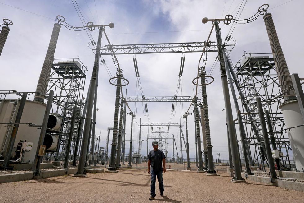 A workman stands outside, dwarfed by electrical substation technology.