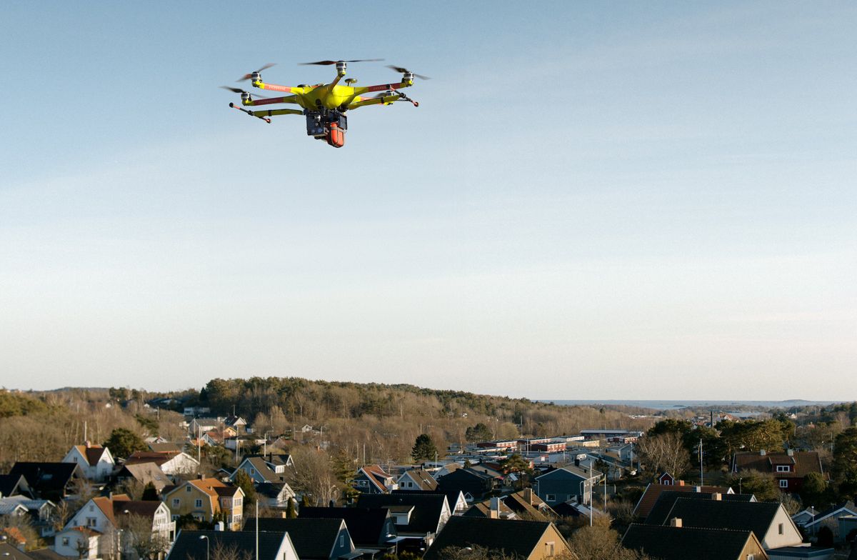 A yellow drone carrying a red AED case 