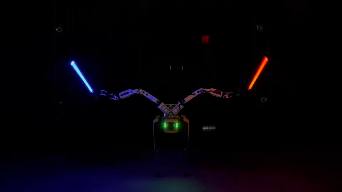 A yellow quadruped robot with two arms attached to its head wields red and blue lightsabers