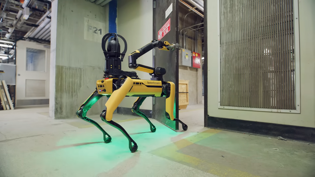 A yellow robot dog with an arm mounted on its head opens a heavy door in an industrial environment