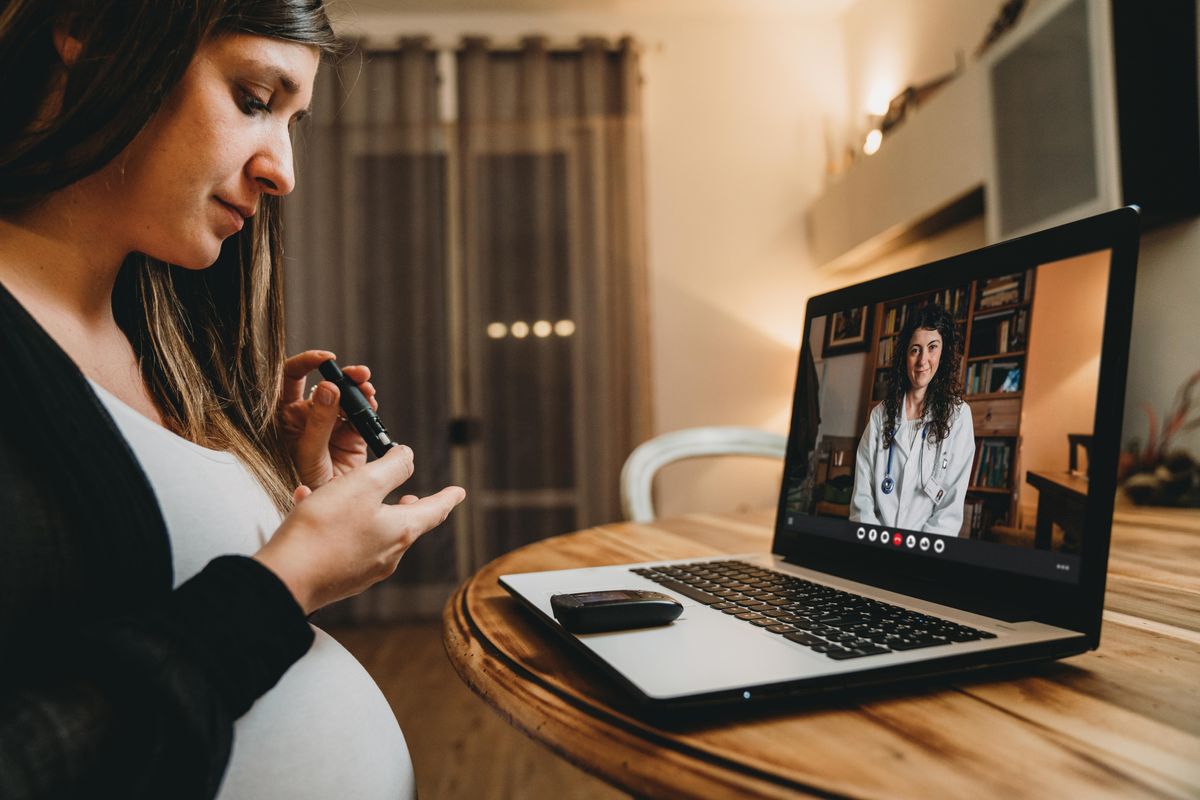 A young pregnant woman is having a video call with her female doctor while she's testing her blood sugar .