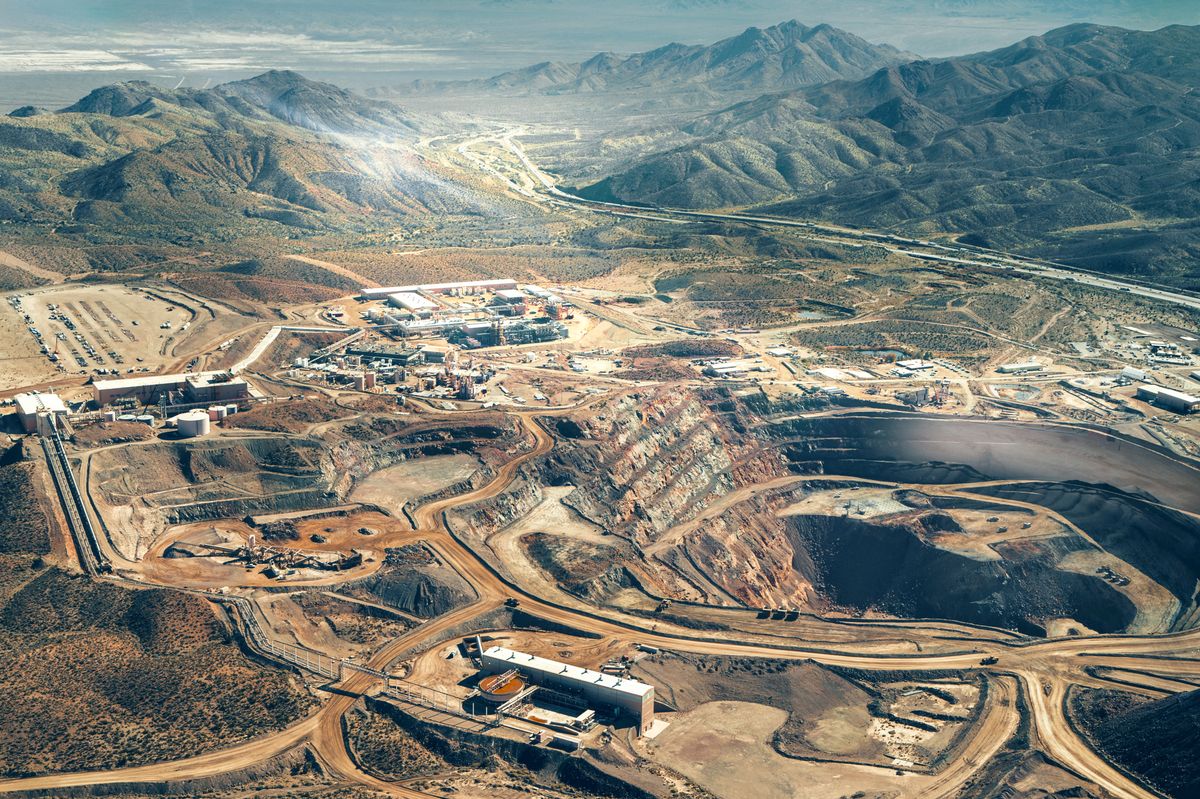 An aerial shot shows dirt roads criss crossing a landscape with mines and mountains. Many large buildings that are small in the overview show the immense scale of the operation.