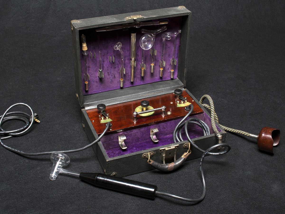 An antique medical apparatus consisting of a black wand, various glass tools to plug into the wand, and a power cord.