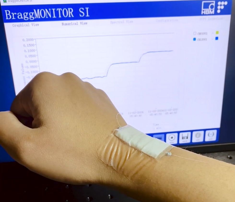 An arm with a rectangular patch moves in front of a screen with a line on it that matches the movement