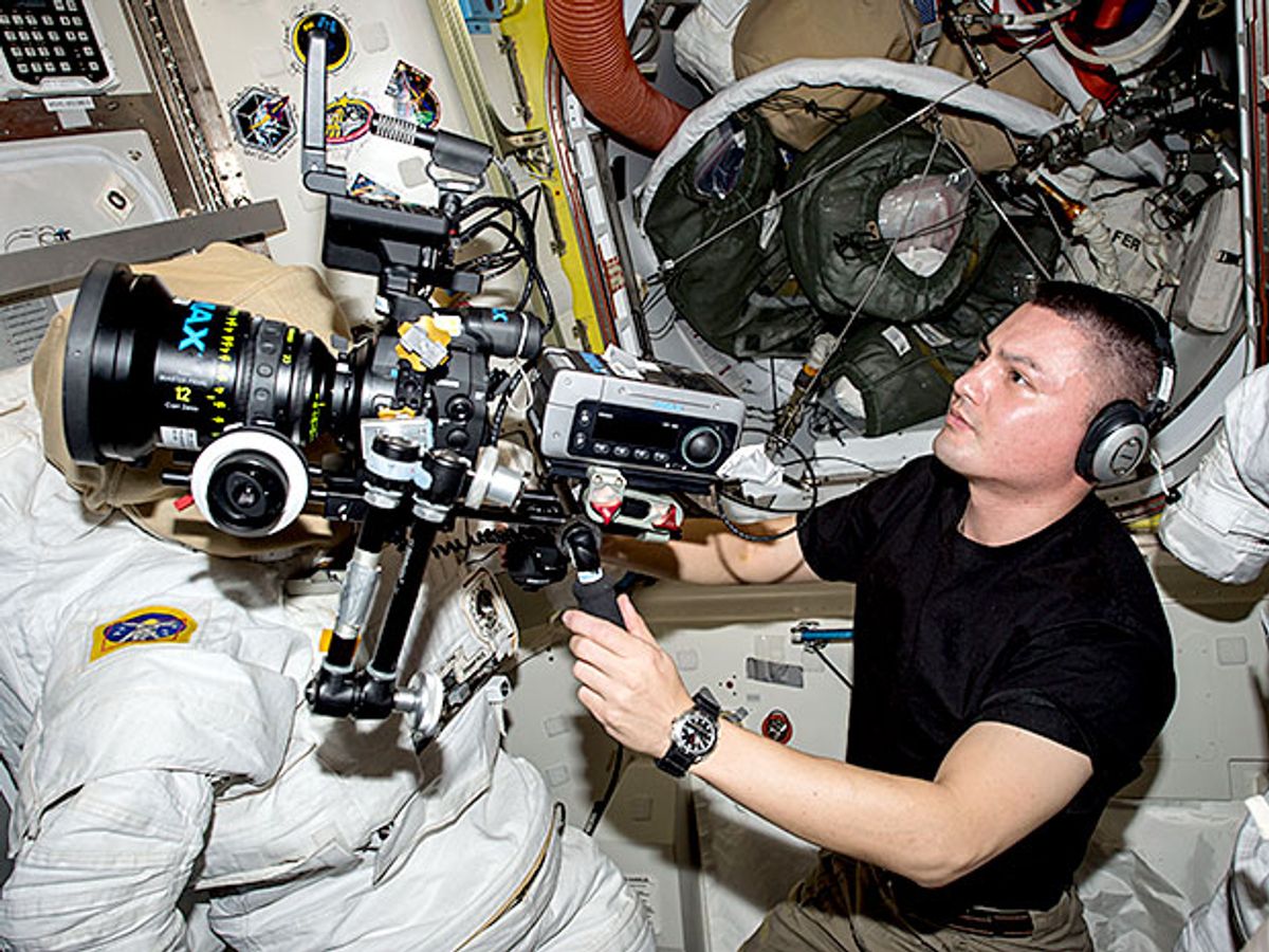 An astronaut floats inside a space station with a sophisticated camera.
