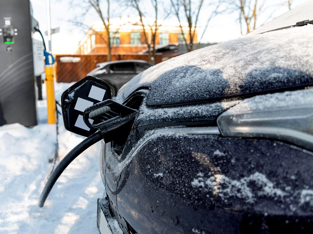 An electric car charging in winter. There is snow and ice on the car and ground.