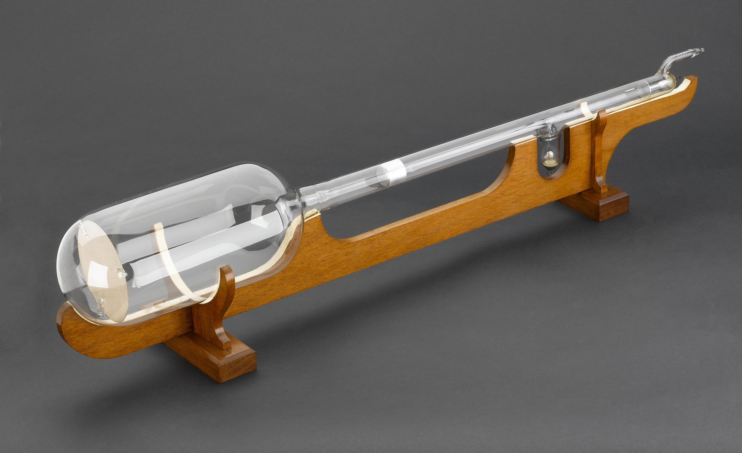 An elongated glass vacuum tube sits lengthwise on a wooden stand.
