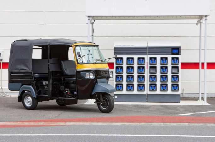 An example of the three-wheeled motorized rickshaws that will be electrified is shown next to a freestanding charging station with a 24-battery capacity.