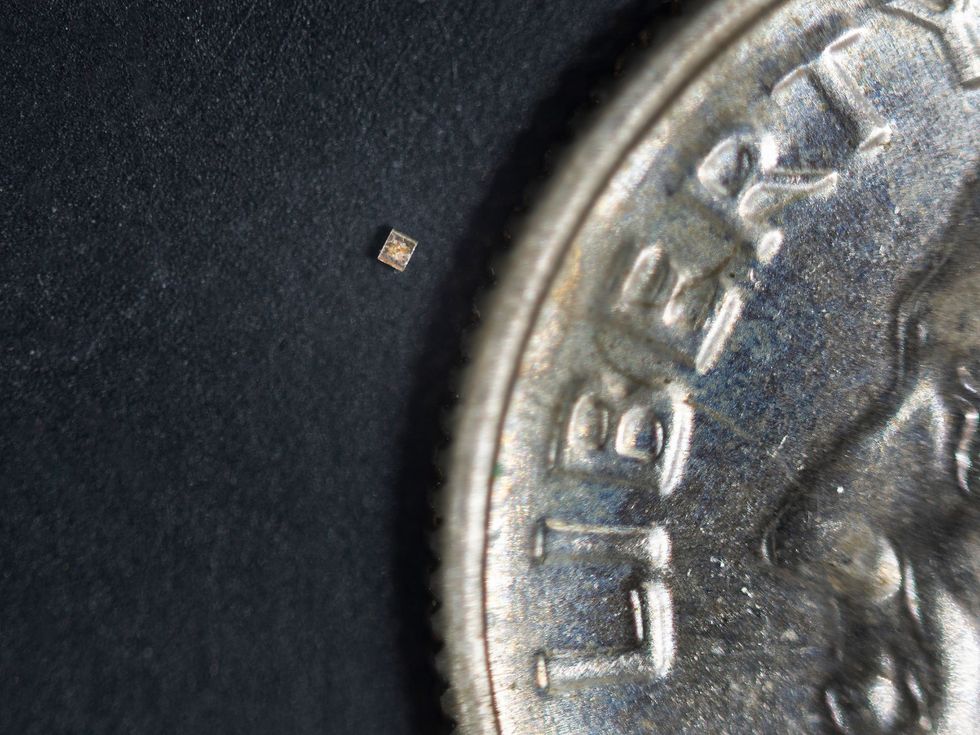 An extreme close-up photograph of a tiny electronic device next to a coin.