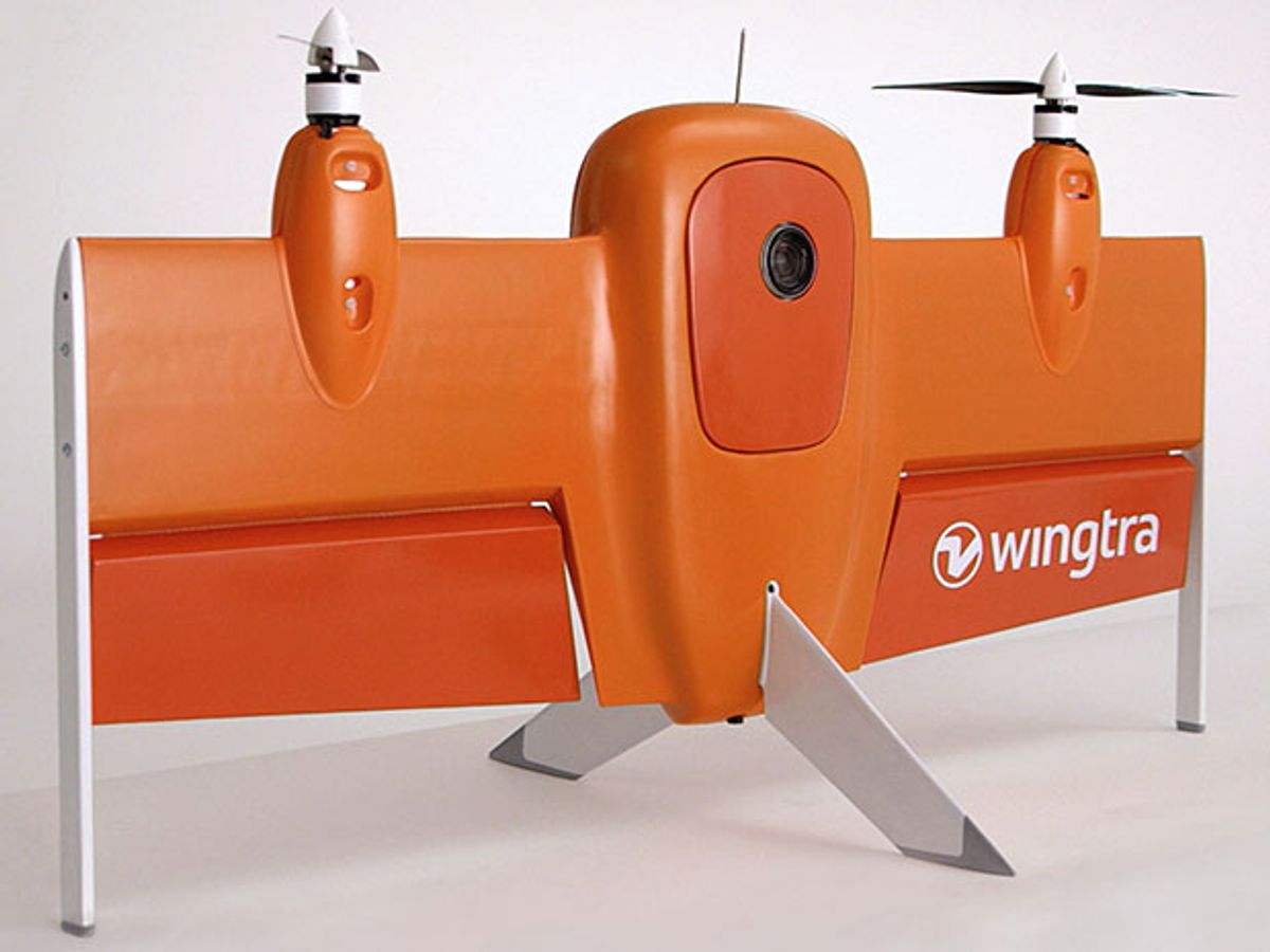 An orange-colored air-plane-shaped drone with two propellers and two large flaps. It is standing vertically, supported by fins from its wings and tail.