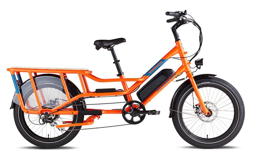 An orange electric bike with thick wheels, a platform over the back wheel and a black electric battery on its frame.