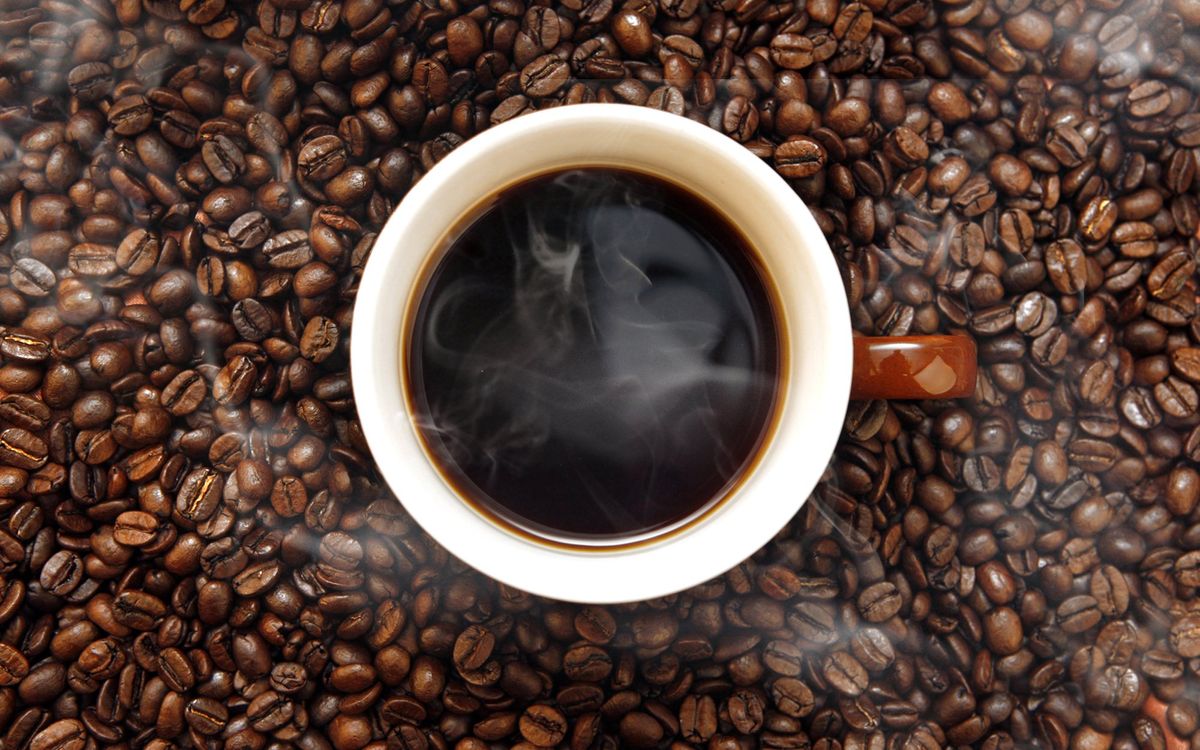 An overhead photograph of a steaming cup of coffee on a background of coffee beans
