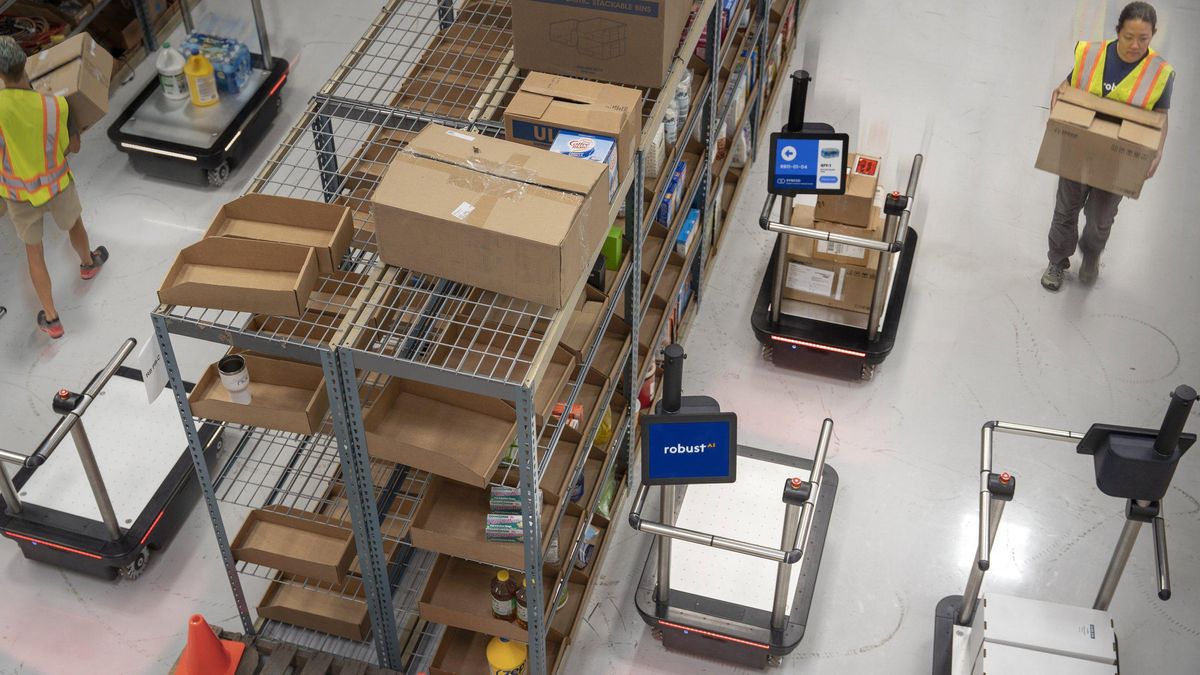 An overhead view of a warehouse showing humans interacting with robotic carts with screens and push bars