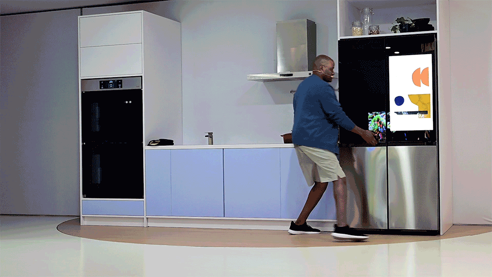 Animated gif of a man moving around a kitchen while a small circular wheeled robot rolls into the frame.