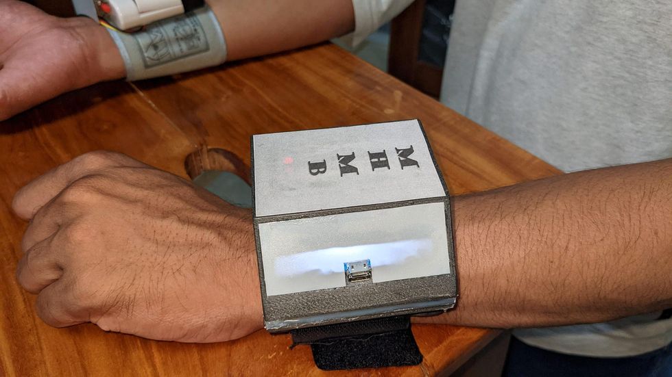 arm with large silver wearable smartwatch on wrist with text reading MHMB