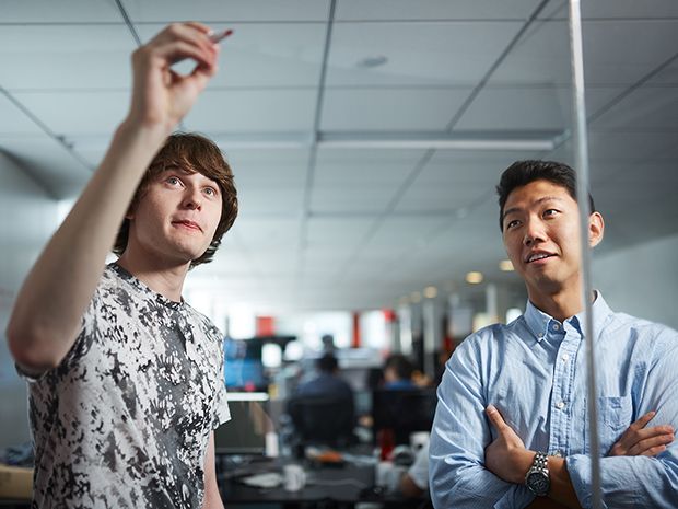 Two employees of Quantopian sketch algorithms onto a glass surface in the company's headquarters.