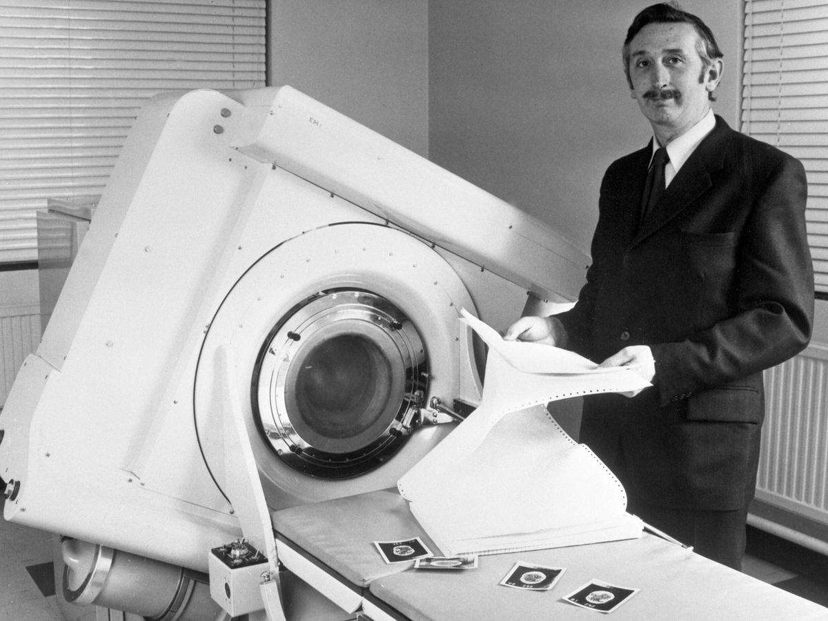 black and white image of a man in a suit standing next to a large x-ray machine