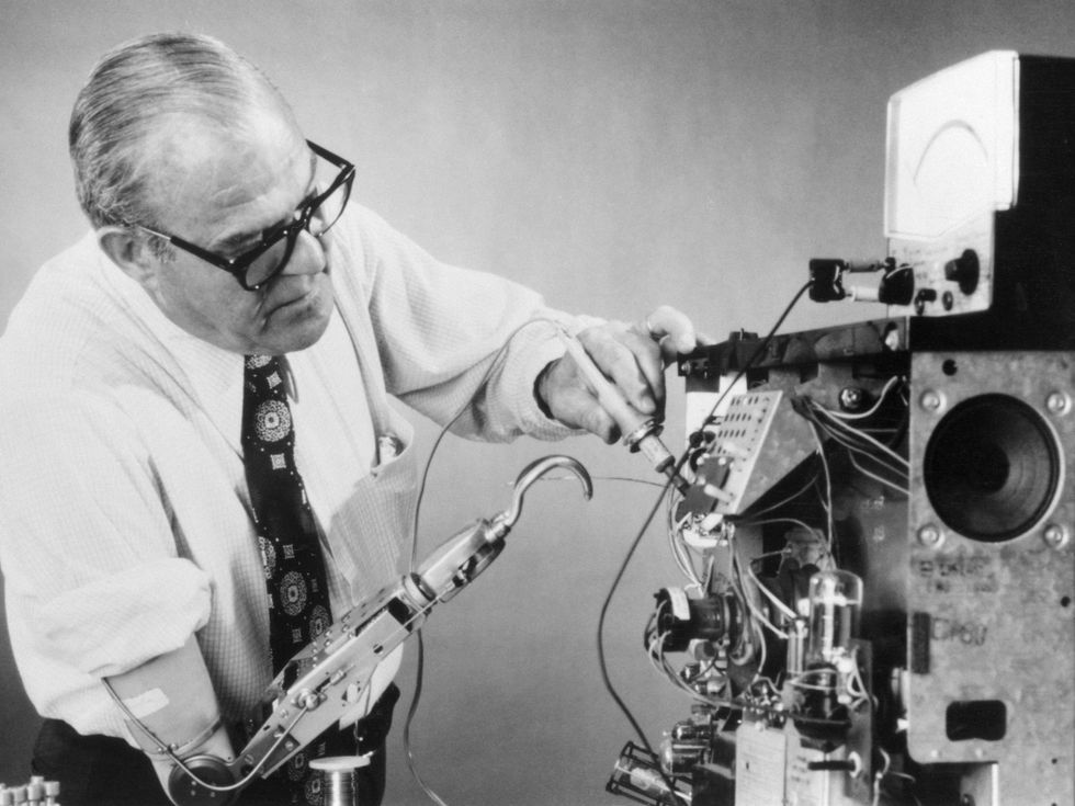 Black and white photo of a man wearing a prosthetic arm and working on electrical equipment.