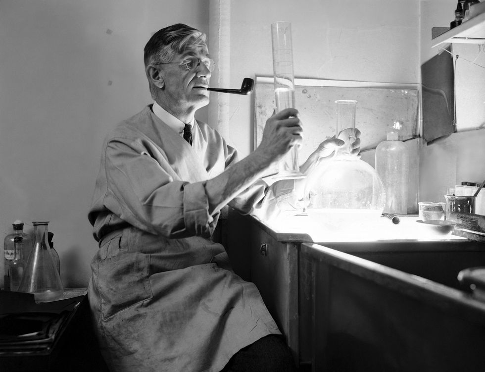 Black and white photo of a man with a pipe holding large test tubes in a lab