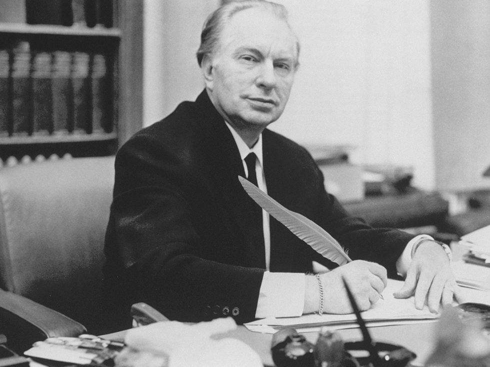 Black-and-white photo of a white middle-aged man in a suit sitting at a desk.