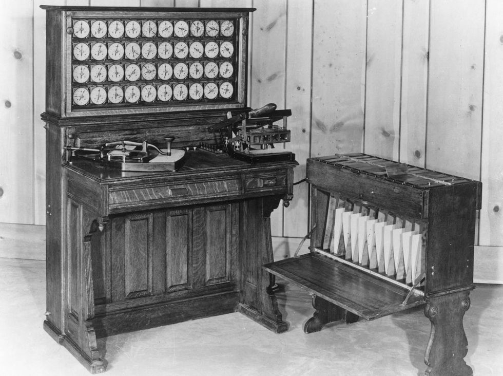 Black and white photo of a wooden apparatus that looks like an upright piano and has rows of round dials across the top.