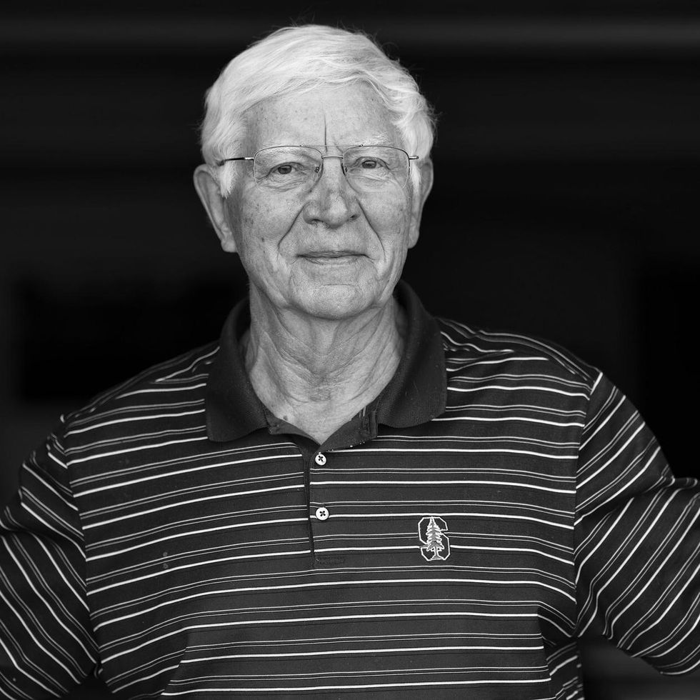 black and white photo of an older man with white hair wearing glasses and a striped shirt