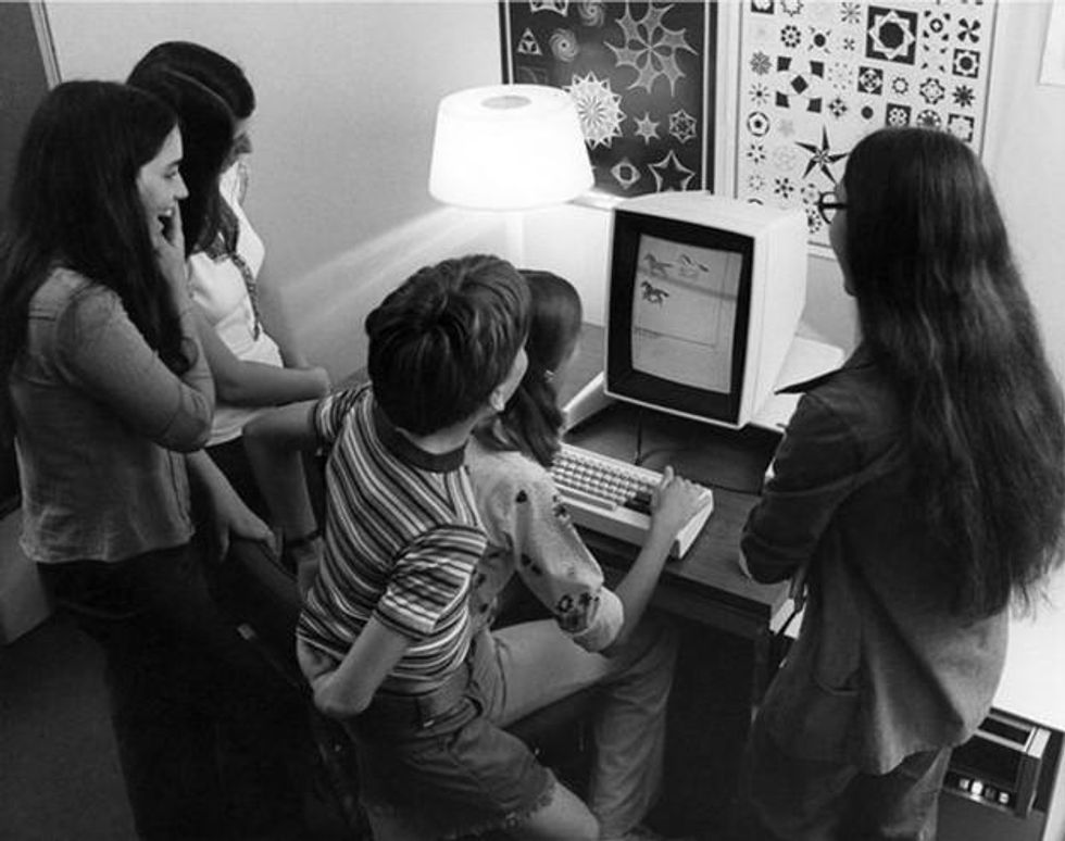 Black and white photo of children sitting in front of an older desktop computer.