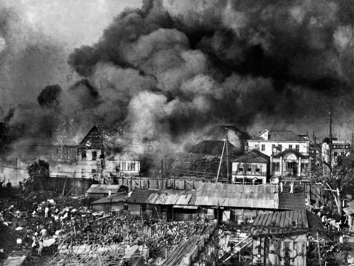 Black and white photo of smoke rising from buildings, some of which are collapsed.