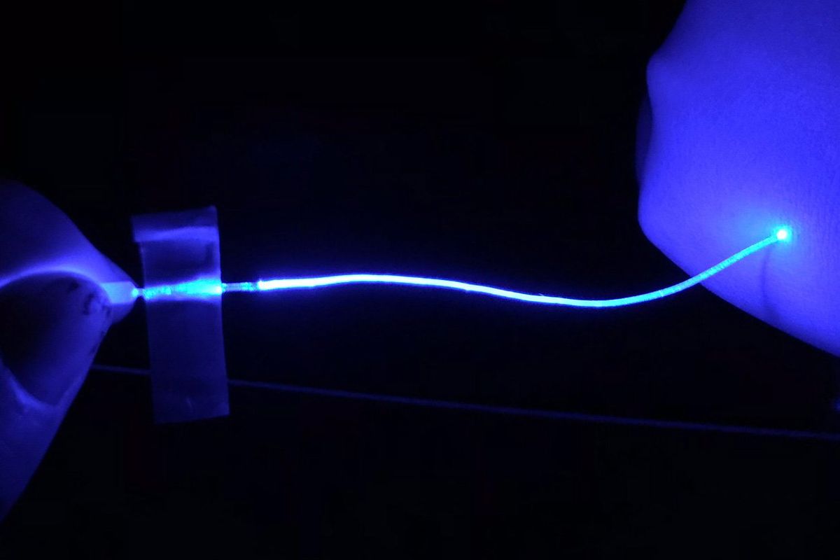 Black background with illuminated blue fiber held by a hand and illuminating a blue object