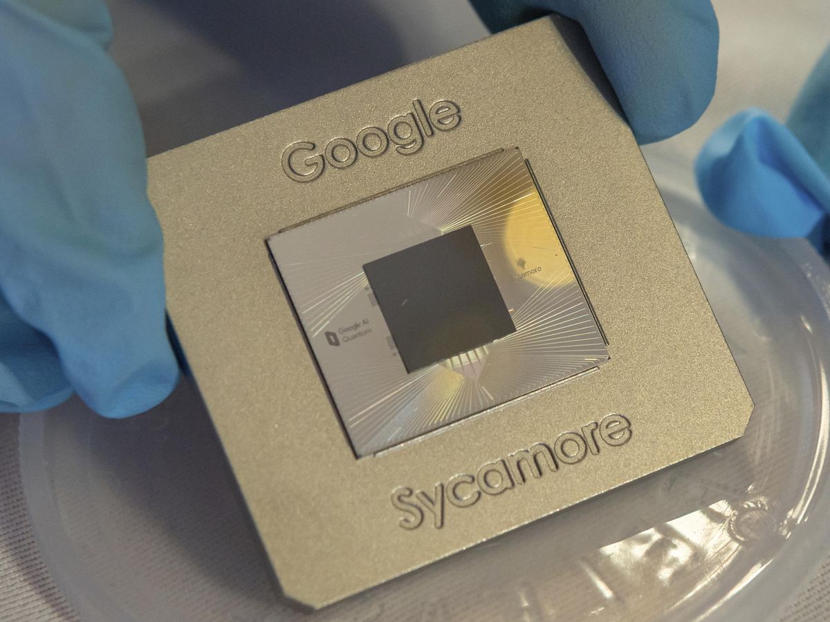 Blue gloved fingers hold up a metallic plate labeled Google Sycamore which houses a square chip