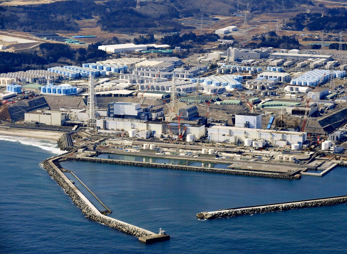 Blue water in the foreground. On land are multiple white buildings and structures. The back third of the photo shows hundreds of white and blue cylindrical tanks grouped together.