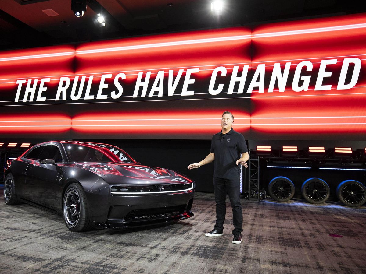 CEO of Dodge Brand standing on a podium next to a Dodge Charger Daytone SRT concept all-electric muscle car. Behind him a giant screen displaying the sentence: The Rules Have Changed.