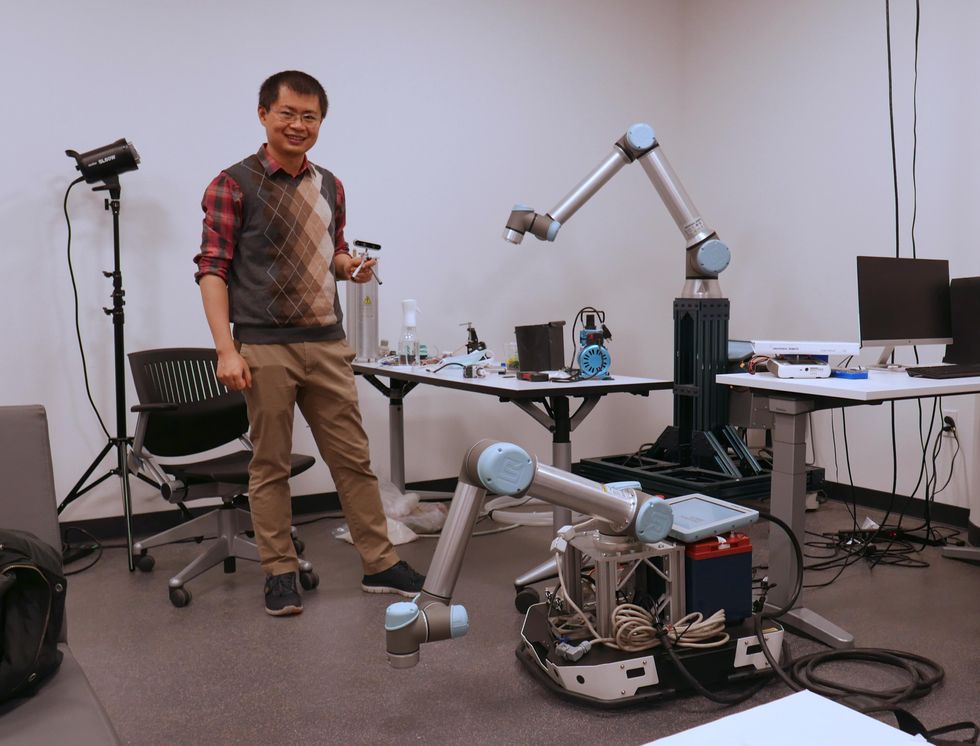 Chen Feng with mobile robots and robot manipulators in his lab.