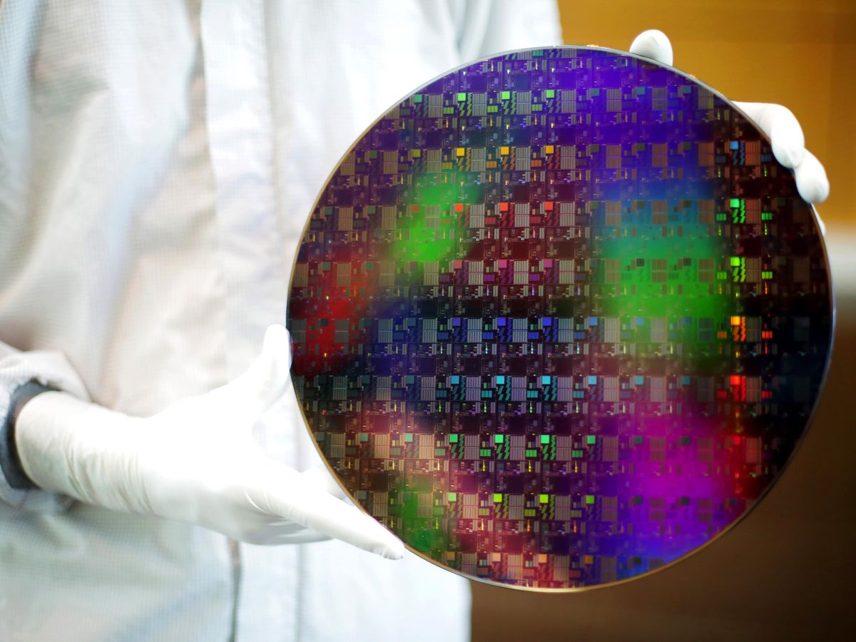 Close-up of a colorful semiconductor wafer held the white gloved hands of a clean room technician.