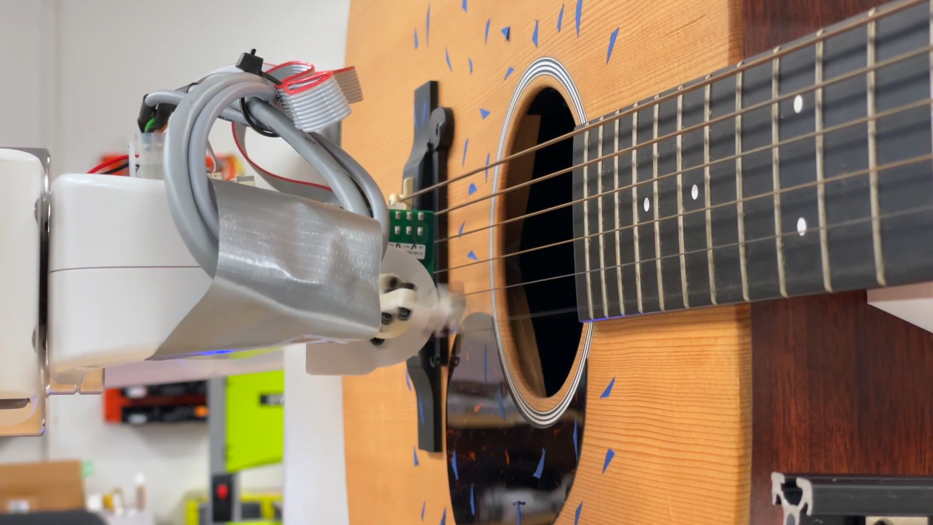Closeup of a robotic arm strumming an acoustic guitar
