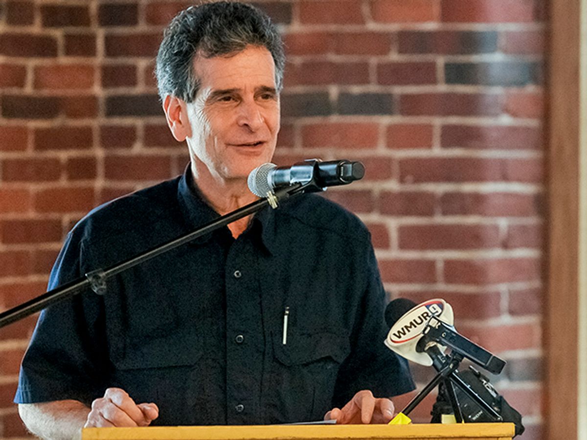 Dean Kamen, dressed in a black button-down shirt, speaking at a lectern