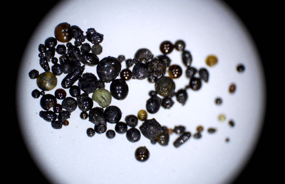 Dozens of shiny oval beads are scatted on a white surface. Most are black, but a few are green or yellow.