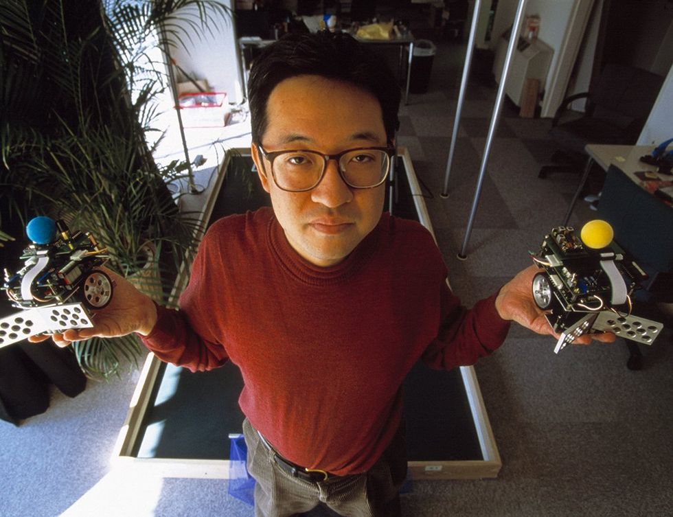Dr Hiroaki Kitano, Japanese artificial intelligence researcher, holding two members of his miniature robot football team.