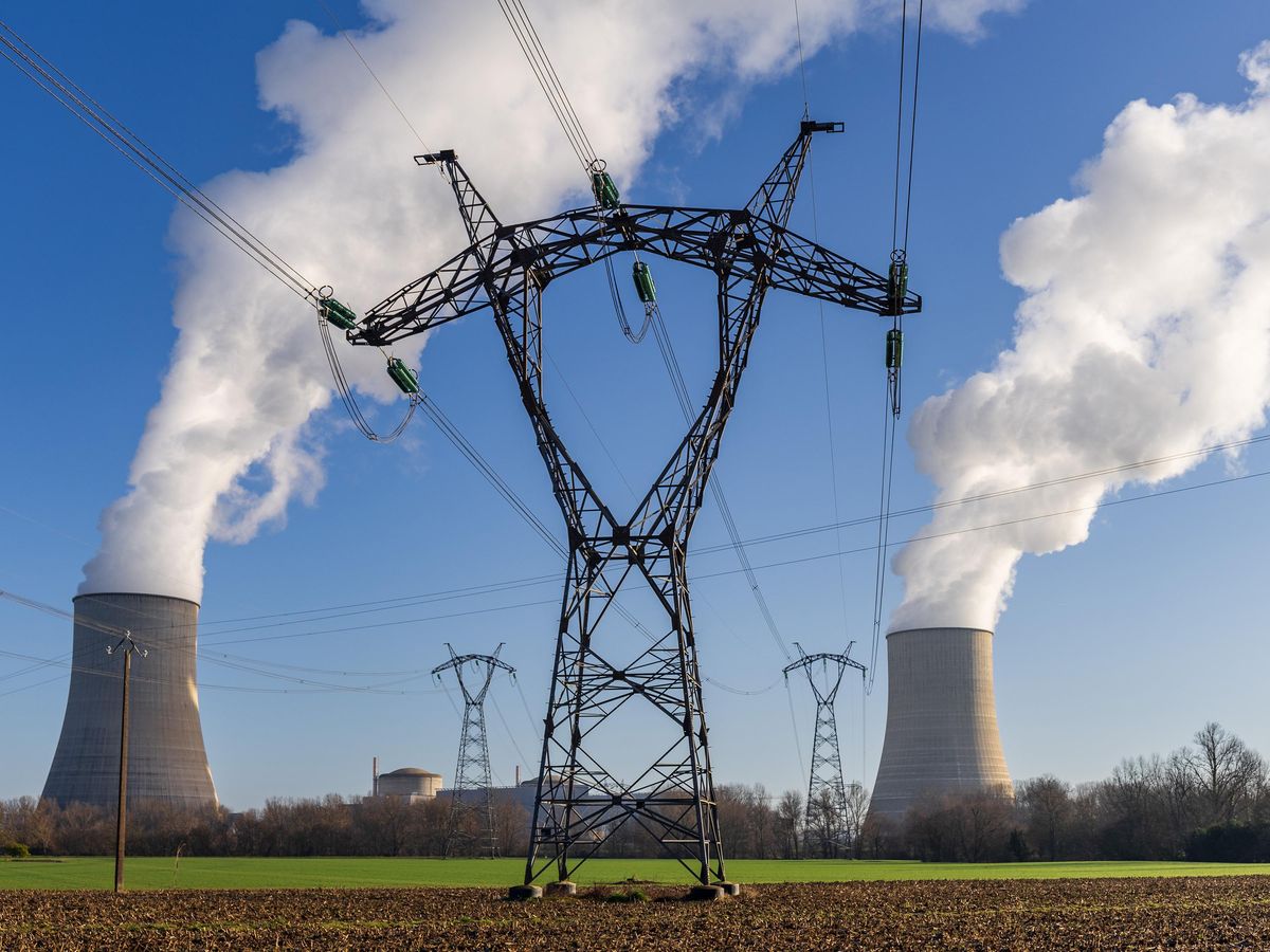 Electricity pylons and power lines stand among nuclear towers with steam rising out of them.