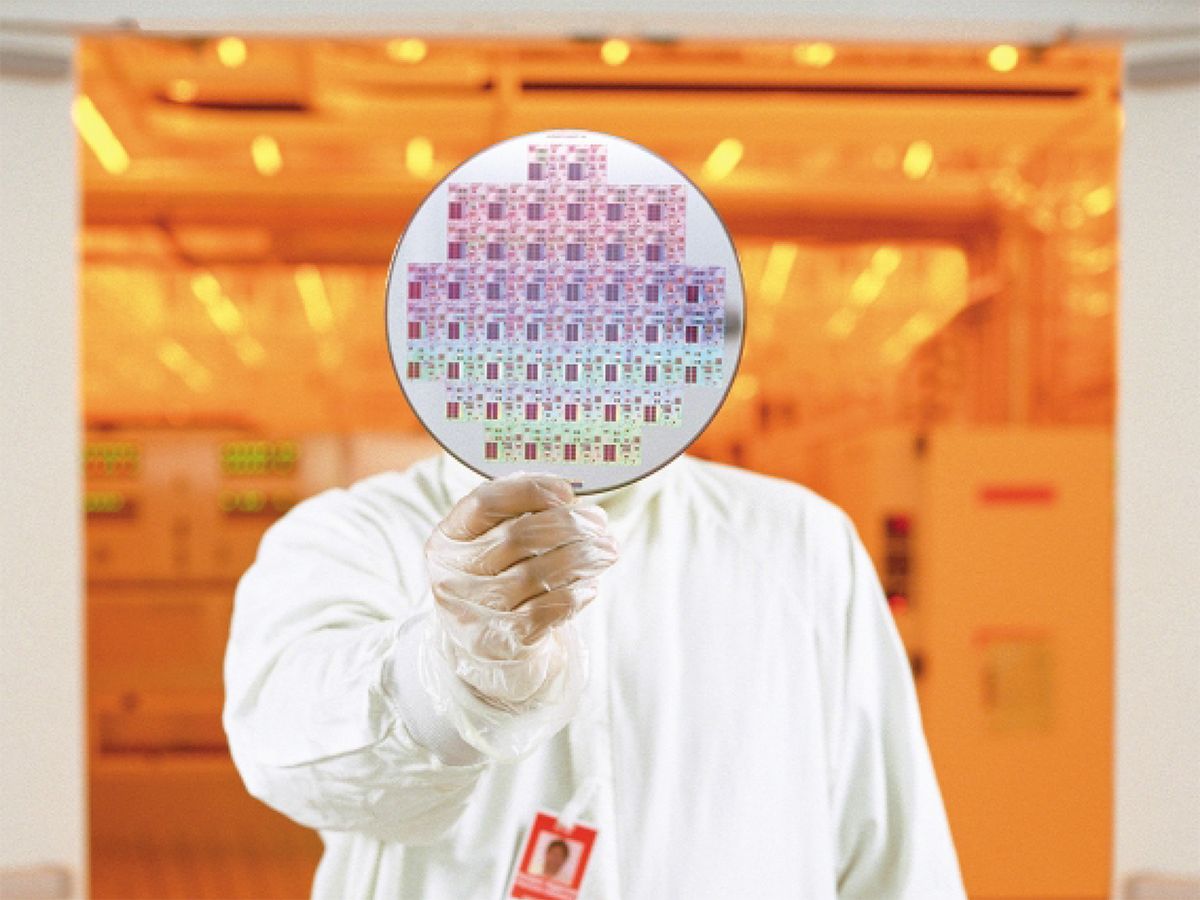 Engineer at Texas Instruments’ Kilby fab in Dallas, Texas, holds up a 200-mm wafer containing developmental 64MB ferroelectric RAM chips.