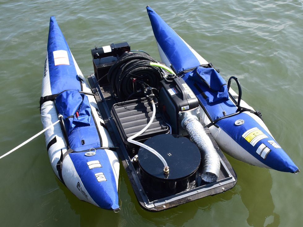 Equipment sits in the center of an open container with a floatation device on each side. The object sits in greenish open water.