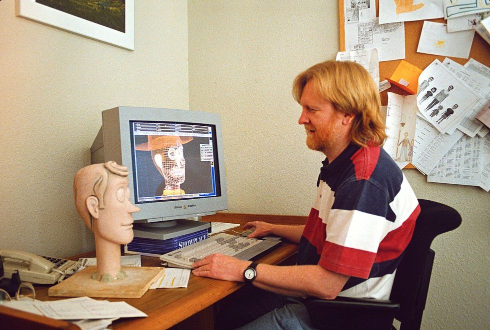 A red haired man sits at a computer with a render of Woody from Toy Story on the screen